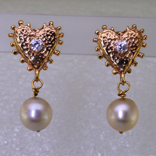 For the gal who loves the nostaligic feel, these one of a kind pearl heart earrings have a vintage feel, with 14 karat yellow gold ornate hearts and beautiful antique ivory pearls that dangle from the bottom. The hearts each have a 3mm cubic ziconia accent in the center, with posts. Measures 1 inch long. 

Made by an unknown artist, and lovingly restored by Stuart J.
