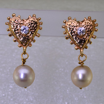 For the gal who loves the nostaligic feel, these one of a kind pearl heart earrings have a vintage feel, with 14 karat yellow gold ornate hearts and beautiful antique ivory pearls that dangle from the bottom. The hearts each have a 3mm cubic ziconia accent in the center, with posts. Measures 1 inch long. 

Made by an unknown artist, and lovingly restored by Stuart J.