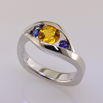 This elegant two color sapphire ring has a low profile, is easy to wear, and super comfy. Priced here in 14 karat white gold with a 1.09 carat sunny yellow round sapphire, and 2 amazing round deep blue sapphires. (We can make it in any metal, and for any size diamond or colored gemstone). This is truly a timeless design, with no prongs to catch. A matching shadow wedding band is also available, if you like this as an engagement ring

This custom designed gemstone ring is individually crafted to be Perfectly You, and is a one of a kind piece. Call us for more information about how we can customize this design Just For You. Designed, and created in our studio by the artist Stuart J.