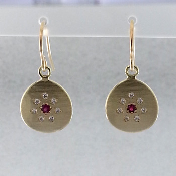 These sweet earrings shimmer when you wear them. Beautiful and rich 18 karat yellow gold medallion drops sprinkled with .11ct. of ideal cut diamonds set in a starburst pattern, with a glowing ruby in the center, hanging from wires. 12mm long.  

Designed and created in our studio by the artist Stuart J.