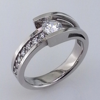 We created this diamond engagement ring design in 950 Palladium, which is a platinum group metal, known for its durability and bright white color. The center diamond of this sparkly, modern ring weighs in at 1/2 a carat. We then jazzed it up with .21 carat total weight of ideal cut diamonds, giving this beautiful engagement ring a classic and timeless look. This beautiful ring will never go out of style, and with no prongs to catch or wear out, is a dream to wear. We can make this ring for any size center, or accent diamonds, including yours. Oh, and we will customize it any way you wish!
Made in our studio by the artist Stuart J.