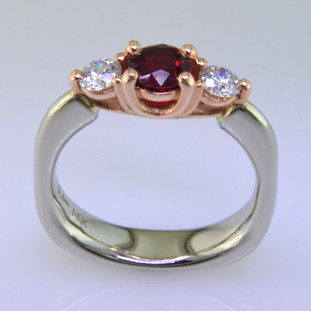 This delicate 3-stone ring is magical. 14 karat White Gold ring shaped with a soft square at the bottom, and 14 karat Rose Gold woven prong work on top. It feels soft and comfy on your finger. Set in the center is a .59ct. beautiful red ruby gemstone, and the sides total .34ct T.W. Ideal cut Diamonds.

Finger size 6 1/2. Can be sized, or custom made in your size. By special order only.  Please allow 4-6 weeks.

Designed, and created in our studio by the artist Stuart J.