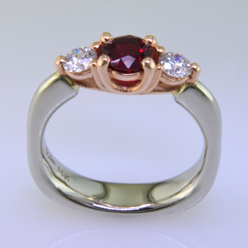 This delicate 3-stone ring is magical. 14 karat White Gold ring shaped with a soft square at the bottom, and 14 karat Rose Gold woven prong work on top. It feels soft and comfy on your finger. Set in the center is a .59ct. beautiful red ruby gemstone, and the sides total .34ct T.W. Ideal cut Diamonds.

Finger size 6 1/2. Can be sized, or custom made in your size. By special order only.  Please allow 4-6 weeks.

Designed, and created in our studio by the artist Stuart J.