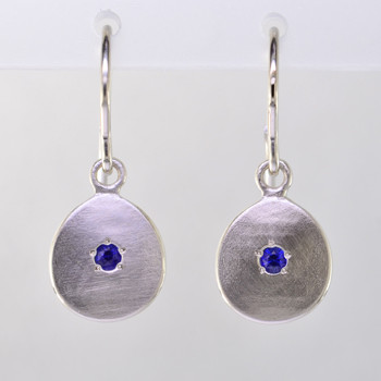 These sweet gemstone earrings shimmer when you wear them. Beautiful in 14 Karat white gold, these medallions with dreamy blue sapphire gemstones in the center, hanging from 14 karat white gold wires.  Earrings measure 3/4 inch long. Available in other colors. Please call for pricing.

Designed and created in our studio by the artist Stuart J.