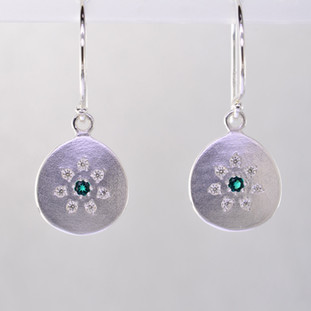 These sweet earrings have a special, hand applied finish that shimmers when you wear it. Beautiful and rich tarnish free sterling silver, sprinkled with .11 carat total weight of ideal cut diamonds, with glowing chatham created emerald gemstones(2mm) in the center. Dangles on sterling silver wires and measures 1 inch long. Available in other colors.  Please call for pricing. 

Designed and created in our studio by the artist Stuart J.

Chatham Gemstones are also available in Ruby, Sapphire, and Alexandrite.

 

                                                                                                                                                                                                                                                                                                                                                                               Chatham® Created Gemstones are grown in carefully controlled laboratory conditions. They are chemically and optically identical to their natural counterparts, yet cost much less. Because the environment in which they are grown is controlled, the imperfections often found in natural gemstones, are absent in Chatham® Created Gemstones. Because of this, and superior cutting, Chatham® gems exhibit the color and sparkle of the finest natural gems. Each one comes with a Certificate of Authenticity, and a Lifetime Warranty.