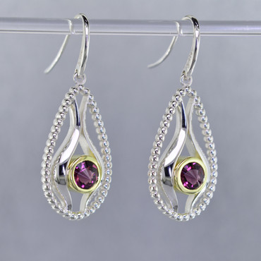 You will be captivated by this mix of modern and vintage in these elegant earrings.  The mix of sterling silver and 18K green gold is magical as these earrings comes together. The 18K bezels make these 6mm rhodolite garnet stratus gemstones pop as they are smooth and have a beautiful deep reddish color.The blend of the two metals is sophisticated, and fun, all at the same time. Perfect for any time of the day or night. These earrings hangs on sterling silver ear wires. The earrings measure 1 1/2 inches long.

Designed, and created in our studio by the artist Stuart J.