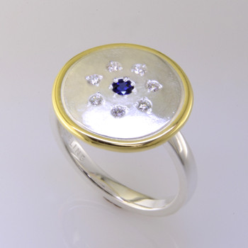 This sweet ring has a special, hand applied finish that shimmers when you wear it. Crafted in beautiful sterling silver, and framed in rich 18 karat yellow gold. It is sprinkled with 7 ideal cut diamonds weighing a tenth of a carat, with a Chatham® created deep blue sapphire gemstone in the center. This one is a size 7, but we can make it in any size. Ring top measures 5/8 inch in diameter.  

Chatham Gemstones are also available in Ruby, Sapphire, and Alexandrite.

Designed and created in our studio by the artist Stuart J.

Chatham® Created Gemstones are grown in carefully controlled laboratory conditions. They are chemically and optically identical to their natural counterparts, yet cost much less. Because the environment in which they are grown is controlled, the imperfections often found in natural gemstones, are absent in Chatham® Created Gemstones. Because of this, and superior cutting, Chatham® gems exhibit the color and sparkle of the finest natural gems. Each one comes with a Certificate of Authenticity, and a Lifetime Warranty.