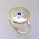 This sweet ring has a special, hand applied finish that shimmers when you wear it. Crafted in beautiful sterling silver, and framed in rich 18 karat yellow gold. It is sprinkled with 7 ideal cut diamonds weighing a tenth of a carat, with a Chatham® created deep blue sapphire gemstone in the center. This one is a size 7, but we can make it in any size. Ring top measures 5/8 inch in diameter.  

Chatham Gemstones are also available in Ruby, Sapphire, and Alexandrite.

Designed and created in our studio by the artist Stuart J.

Chatham® Created Gemstones are grown in carefully controlled laboratory conditions. They are chemically and optically identical to their natural counterparts, yet cost much less. Because the environment in which they are grown is controlled, the imperfections often found in natural gemstones, are absent in Chatham® Created Gemstones. Because of this, and superior cutting, Chatham® gems exhibit the color and sparkle of the finest natural gems. Each one comes with a Certificate of Authenticity, and a Lifetime Warranty.