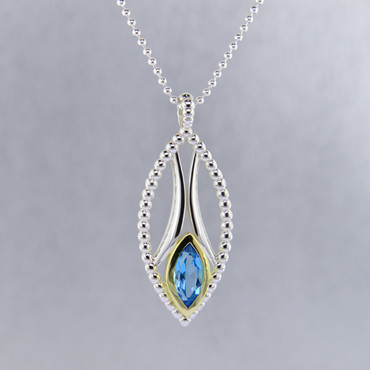 You will be captivated by this mix of modern and vintage in this elegant pendant. The mix of sterling silver and 18 karat green gold is magical as this pendant comes together. The 18 karat bezel make this beautiful 12x6mm marquise Swiss blue topaz gemstone pop. The blend of the two metals is sophisticated, and fun, all at the same time. Perfect for any time of the day or night. This pendant hangs on a sterling silver bead chain, 24" long. The pendant measures 1 3/4 inches long.

Designed and created in our studio by the artist Stuart J.