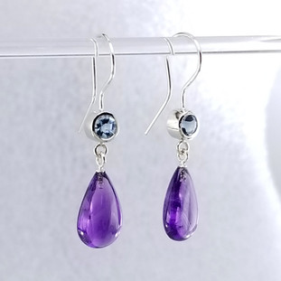 We picked these beautiful Zambian Amethyst drops because the color was so rich! We added beautiful light Blue Topaz for a perfect match. Handmade in 14 karat white gold, with blue topaz buff top gems set in bezels, and the amazing deep purple amethyst drops, making these earrings the perfect accessory to any outfit! These drop dangle earrings measure 1 1/4" long, and hang on 14 karat white gold wires.

Designed and created in our studio, by the artist Stuart J. Adelman.