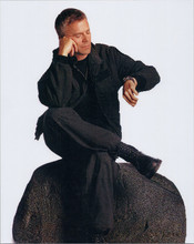 Richard Dean Anderson looks at his watch MacGyver pose seated on rock 8x10 photo
