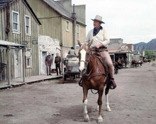 John Wayne sits on horse riding through western town unknown movie 8x10 photo