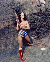 Lynda Carter as TV's Wonder Woman holding up rifle standing by wall 8x10 photo