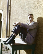 Rock Hudson early 1960's candid leans against wall sat on table 8x10 inch photo