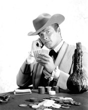 Roger Moore holds up cards as Beau Maverick at gaming table 8x10 inch photo