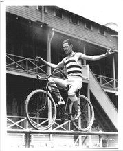 Charley Chase rides his bike along fence 8x10 inch photo