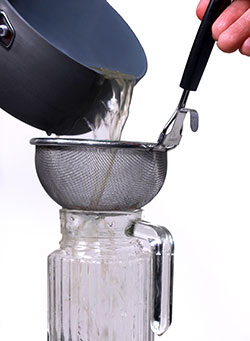 Pouring green coffee extract through a sieve to remove the coffee beans