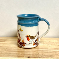 Hand-thrown mug with self-printed sepia toned decals including birds, wheat and other plants applied after glaze firing. A great combination of shadow blue above the cream bird flower combination.  This beautiful round mug stands 4.5 in high by 3.5 in wide and holds about 14 oz of liquid.  Each mug will be unique.