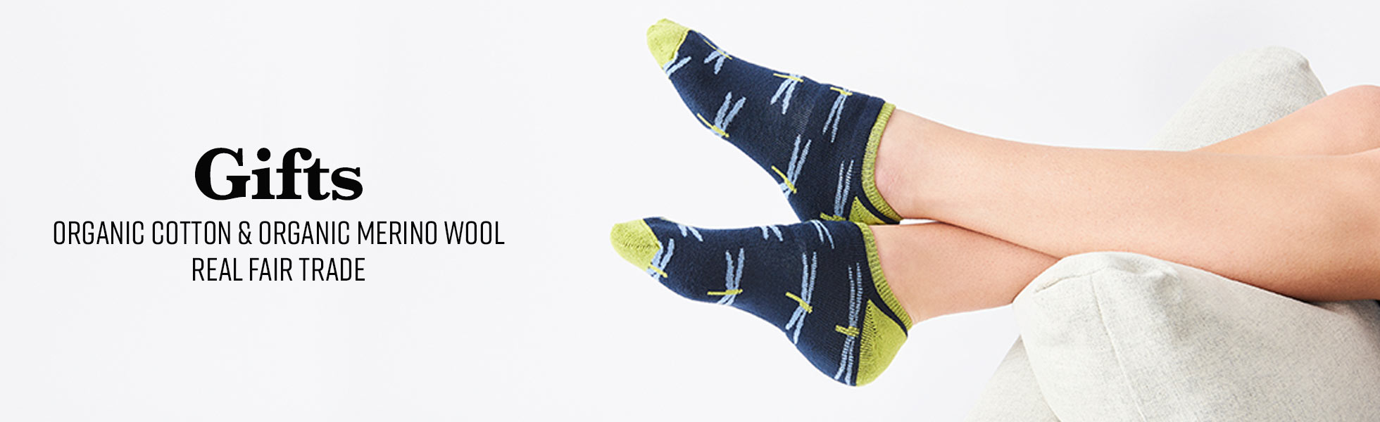 Person wearing Navy Dragonfly Biodiversity Footie Sock. Text next to them reads: Gifts Organic Cotton and Organic Merino Wool Real Fair Trade.