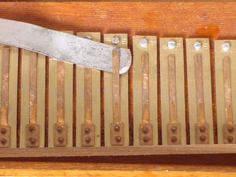 A thin knife blade slid under a harmonium reed tongue