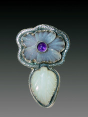 If you are an avid Amy Kahn Russell collector, don't miss this example of her carved flower line! This beautiful Amy Kahn Russell pin/pendant features a large hand-carved agate flower centered with an amethyst cabochon, resting on a hand-carved pale green jade leaf. The flower is set in an elaborate silver embellished frame and the entire pin is bezel set in sterling silver. 2-3/4" x 2" 