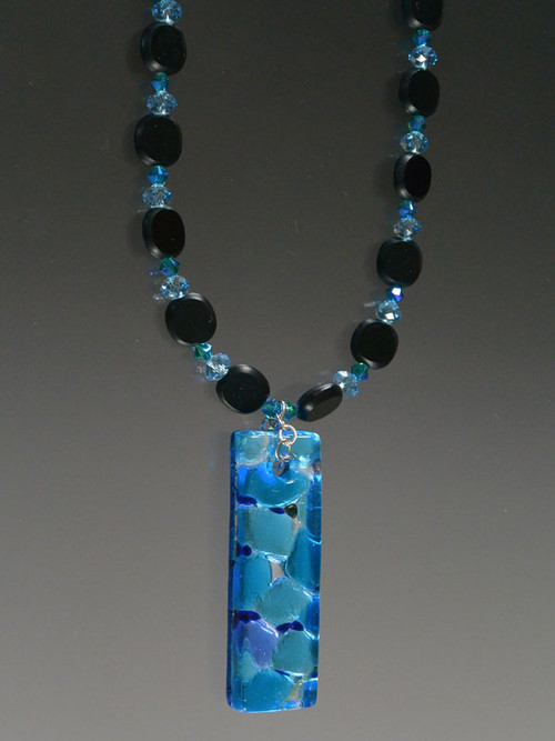 This dramatic necklace features jet glass, swarovski crystals, and a dichroic aqua blue square pendant. 22"