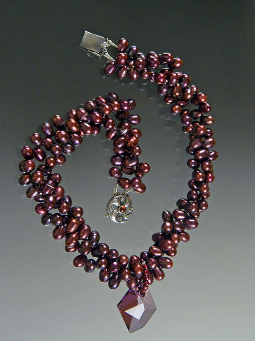 This luxurious bold collar features multi strands of tiny top drilled wine freshwater pearls  and a "cosmic" Swarovski crystal pendant with unique facets that brilliantly reflect light and color like no other pendant in the world (a perfect example of why Austrian crystal can never be duplicated).  A sterling amethyst pearl  clasp completes the picture. 20" 17-1/2" twisted. Pendant 1-1/2" ONE OF A KIND