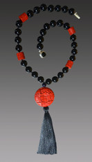 I discovered this stunning deeply hand-carved cinnabar focal bead many years ago in San Francisco.  It forms the basis of this rare and dramatic necklace that features black Venetian glass and barrel shaped complementary carved red cinnabar beads finished off with a luxurious black silk tassel. Totally elegant and very limited.  22" Tassel 6.5"