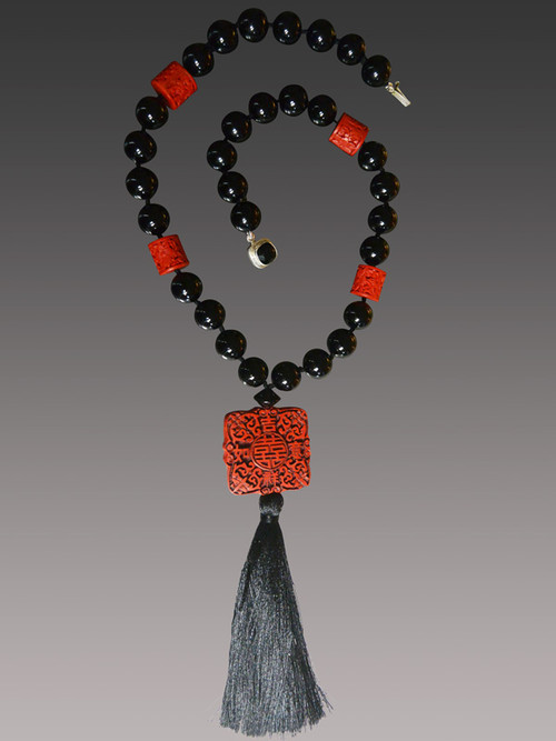 This intricately patterned authentic hand-carved cinnabar square highlights a dramatic necklace featuring Venetian glass and barrel shaped complementary carved red cinnebar beads finished off with a luxurious black silk tassel. Totally elegant and very limited.  22" Tassel 6.5"