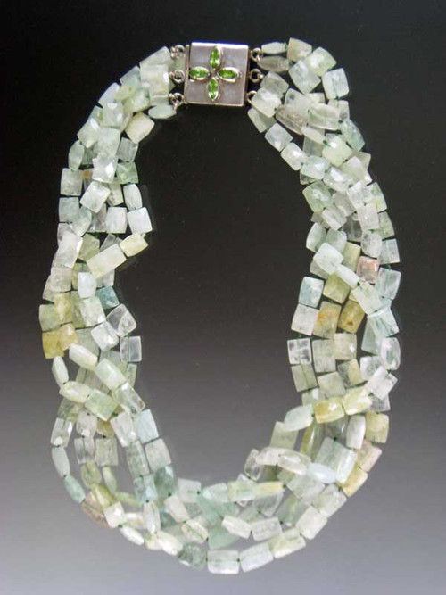 An opulent statement torsade featuring 5 strands of Grade AAA faceted aquamarine rectangles in delicate tones of pale aqua, cloud, and light green blend into a stunning collar with maximum impact. Hand-knotted with aqua silk. A custom clasp of marquis shaped peridot stones set in sterling silver can be worn as a center or side highlight for added impact. 20"