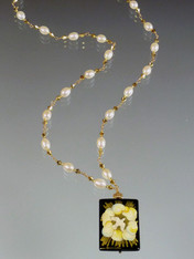 This hand-painted Russian lacquered miniature features a beautiful white dove circled by gold swirling clouds encased in thin gold strips. The black onyx pendant (1" x 3/4") has been painstakingly covered with many layers of oil paint, egg tempura, gold foil, and lacquer to create the dramatic effect.  The pendant, crowned with a 14K gold rondel and 24K Swarovski crystal, hangs from a gold wire wrapped chain of white freshwater pearls and swarovski crytals. 20" 