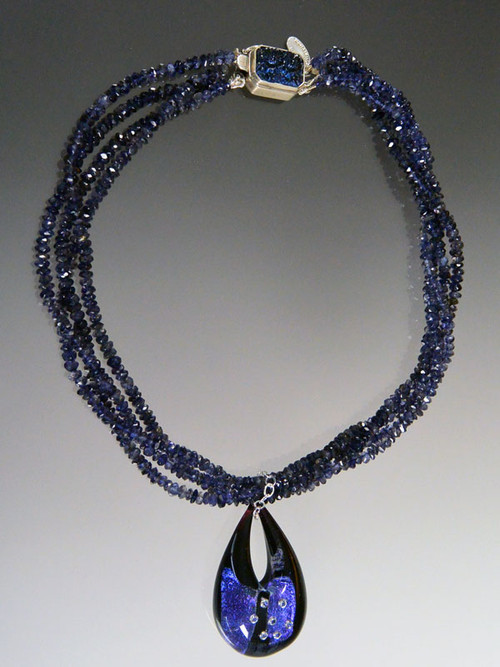 Blue is a big color trend this season and this dazzling necklace has it all - three strands of grade AAA Iolite (a member of the sapphire family) rondels with a custom sterling iolite clasp and a one of a kind authentic Venetian glass pendant in the shape of a teardrop featuring sterling silver over deep blue Murano Glass with sparkling cubic zirconia near the surface.  The entire teardrop is encased in clear Murano Glass giving it a magnified effect. Totally stunning in person with great depth and flashes of color. 22" Pendant 1-1/2" 
