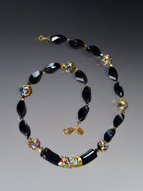 This necklace  features a limited edition 60mm Venetian glass focal curved "Klimt" tube of black Murano Glass with a center exterior section of 24K gold with small bits of embedded millefiori mosaic resembling a Klimt painting. The rest of the necklace features onyx swirls, round Klimt mosaics, and 24K Swarvoski plated beads.  18"
