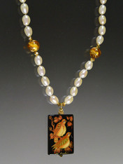 This hand-painted lacquered miniature features two love birds underlit with luminous gold 24K foil. The black onyx pendant (1-1/2" x 1) has been painstakingly covered with many layers of oil paint, egg tempura, gold foil, and lacquer to create the dramatic effect and signed in gold by the artist.  The pendant, crowned with a 14K fluted rondel and 24K Swarovski crystal, hangs from a hand-knotted strand of Grade AA white pearls with topaz gold Venetian stations. 18" 
